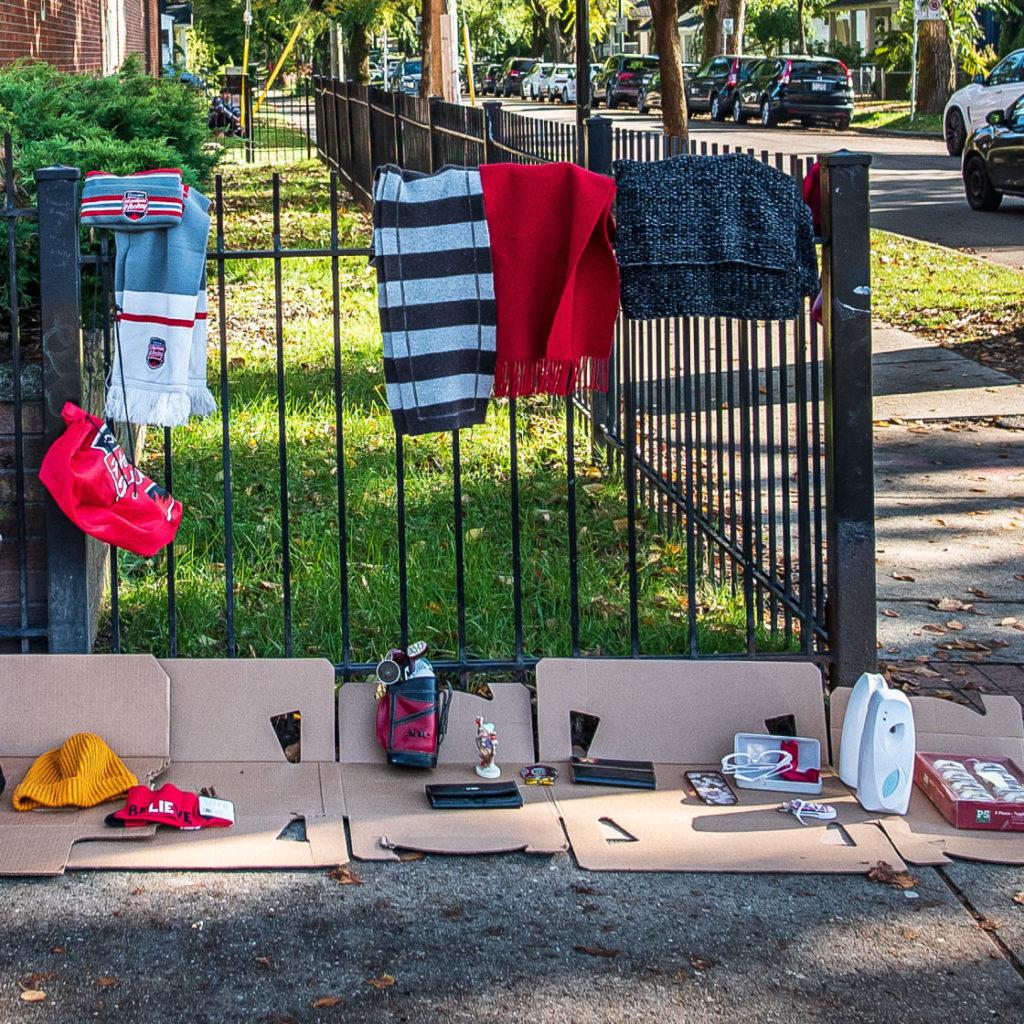 A clothing vendor sells hats and scarves along a sidewalk