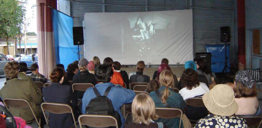 People watching a movie in an autobody shop that has been transformed into an outdoor cinema
