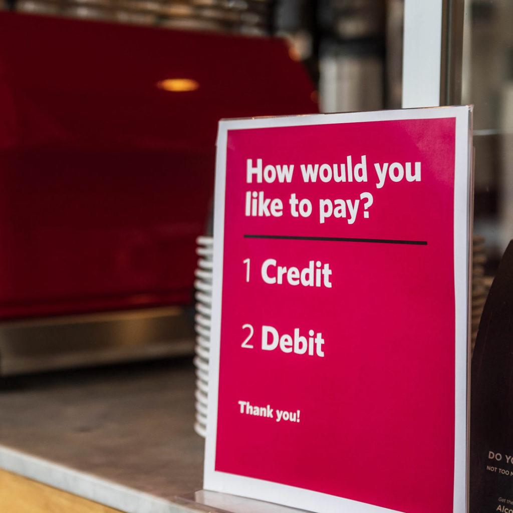 A sign that asks how a patron would like to pay sits on a coffee shop counter