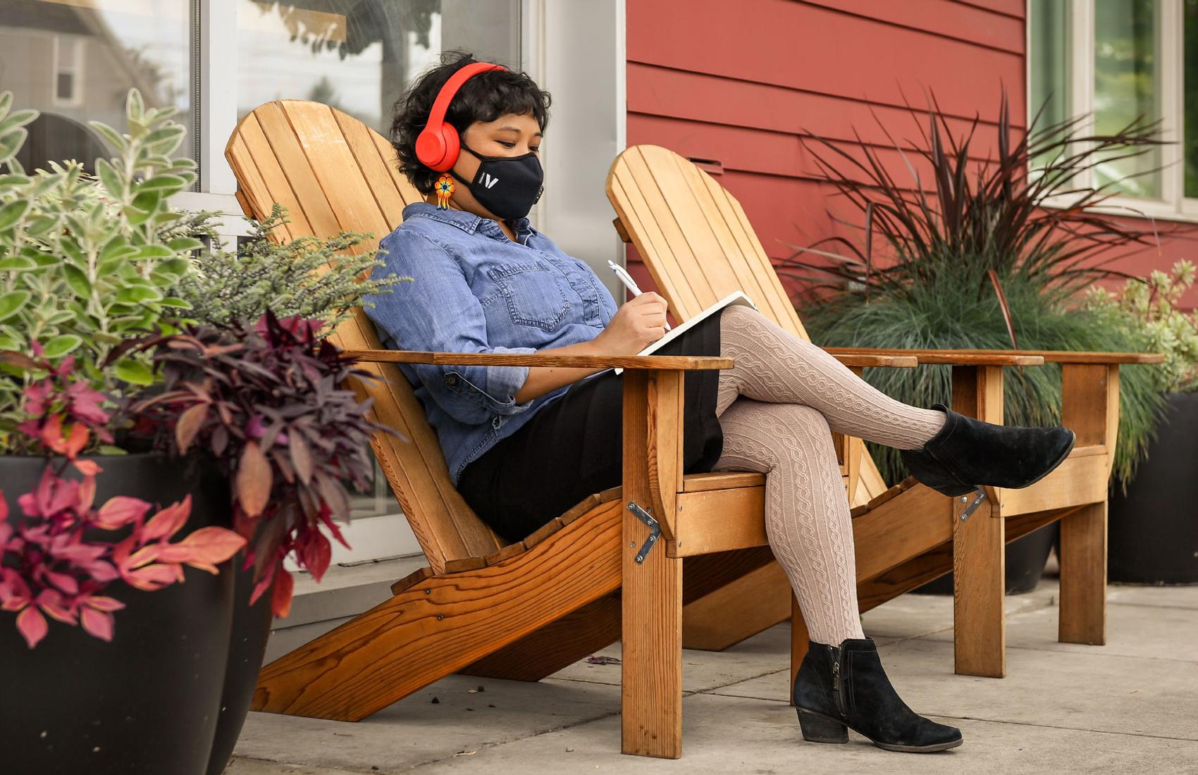 A Filipinx woman with a COVID-19 face mask sits outside and writes in a notebook.