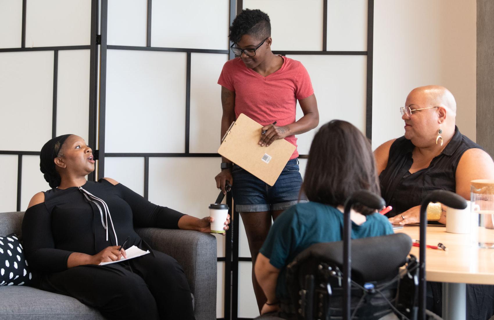 Four disabled people of colour gather around a table during a meeting.