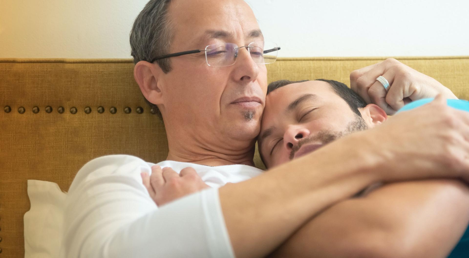 Two men embrace in a bed