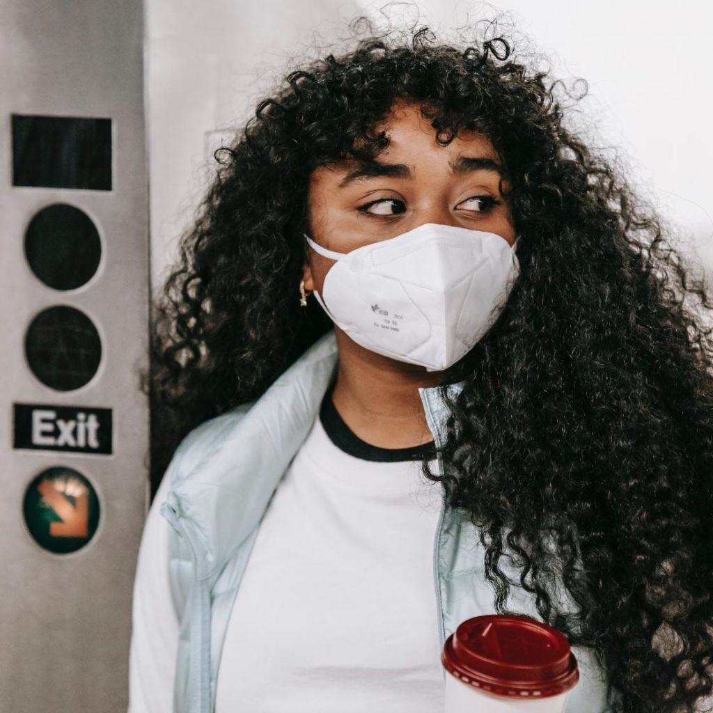 A young women wearing a medical mask enters onto a transit platform. Her face look anxious, as she is worried about re-entry into society after the COVID-19 pandemic.