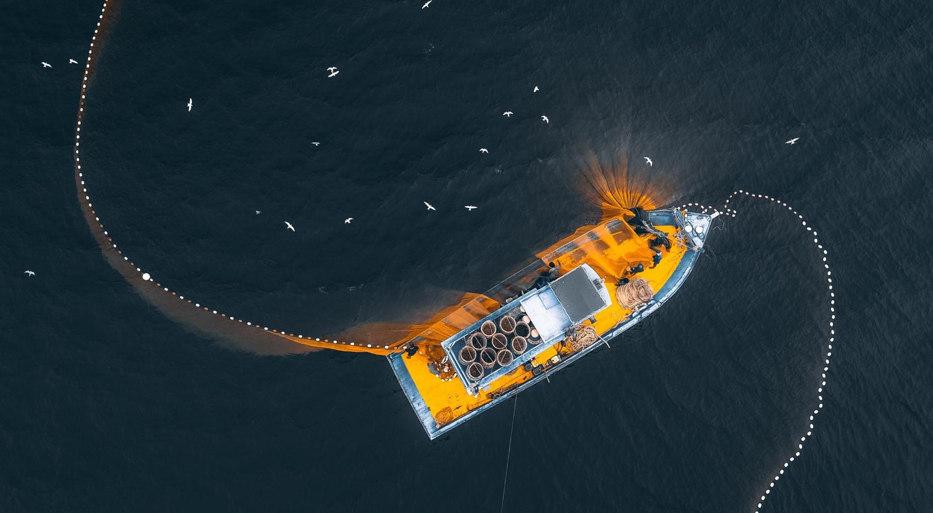 Aerial photo of a fishing trawler in the ocean with its nets cast out into the water to catch fish with