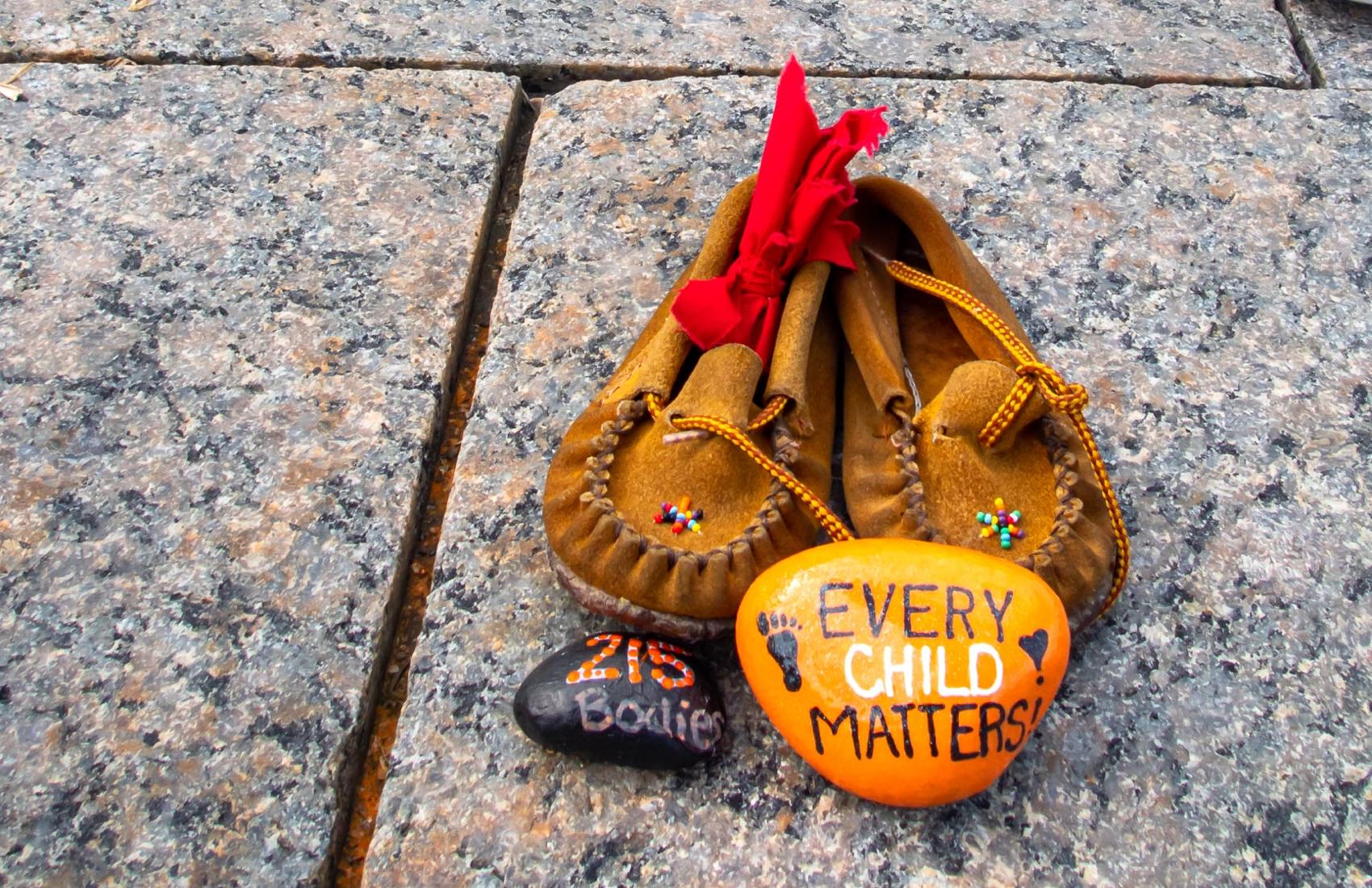 Children's shoes and a painted orange rock that reads "Every Child Matters" site at a memorial at Canada's Parliament Hill for Indigenous children who were sent to Residential Schools