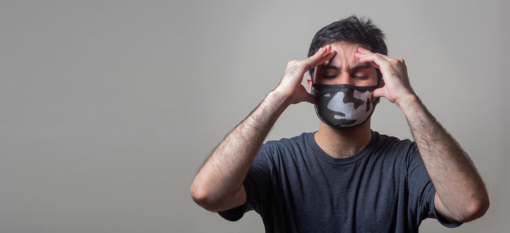 Person on grey background wearing a mask and holding hands on temples