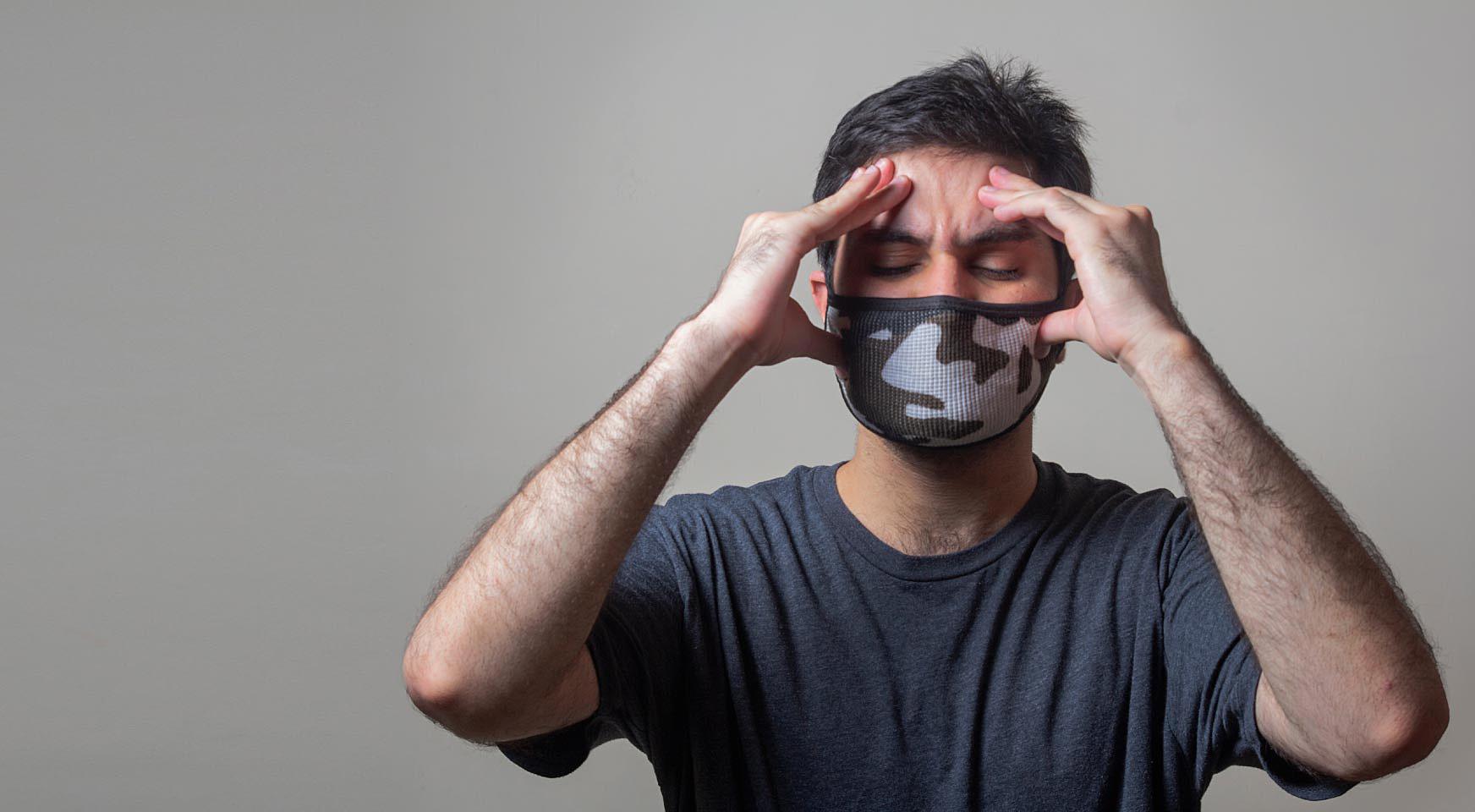 person on grey background wearing a mask and holding hands on temples
