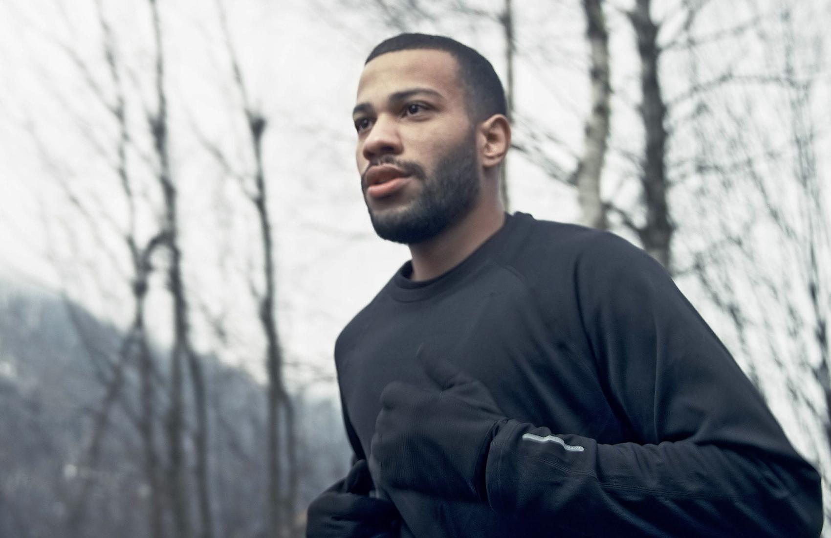 Bearded man running in a forest wearing a black outfit and gloves