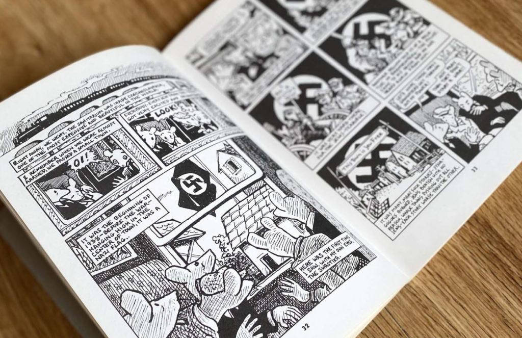 Photo of the book Maus open to a page with mice on a train looking out a window at a swastika on a flag pole.
