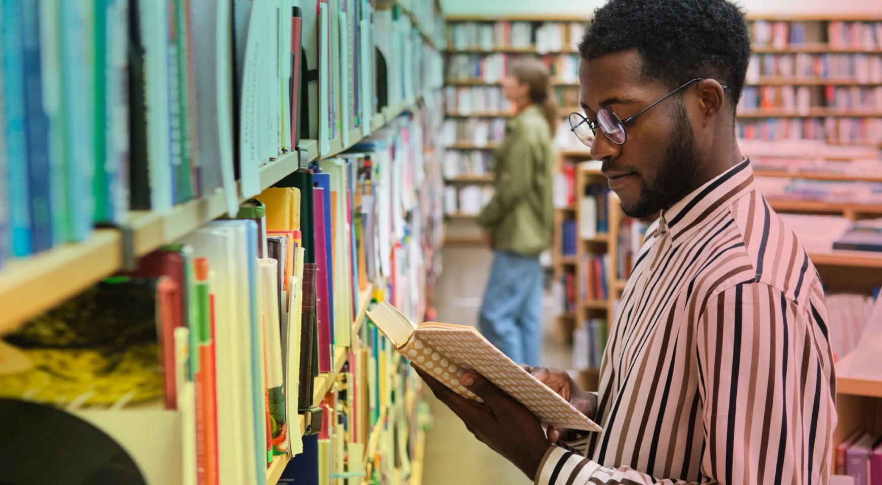 Young man in striped shirt in bookstore holding book and reading