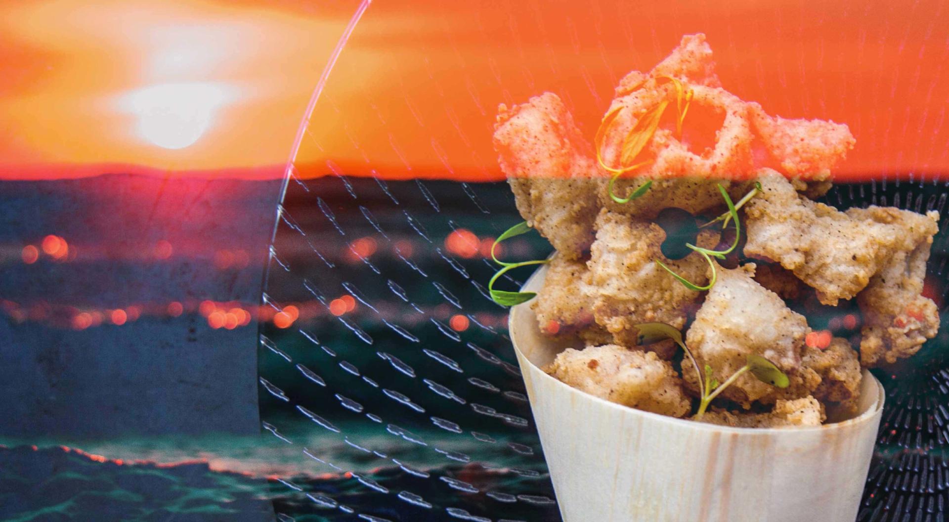 A photo of fried calamari with the ocean and sun in the background