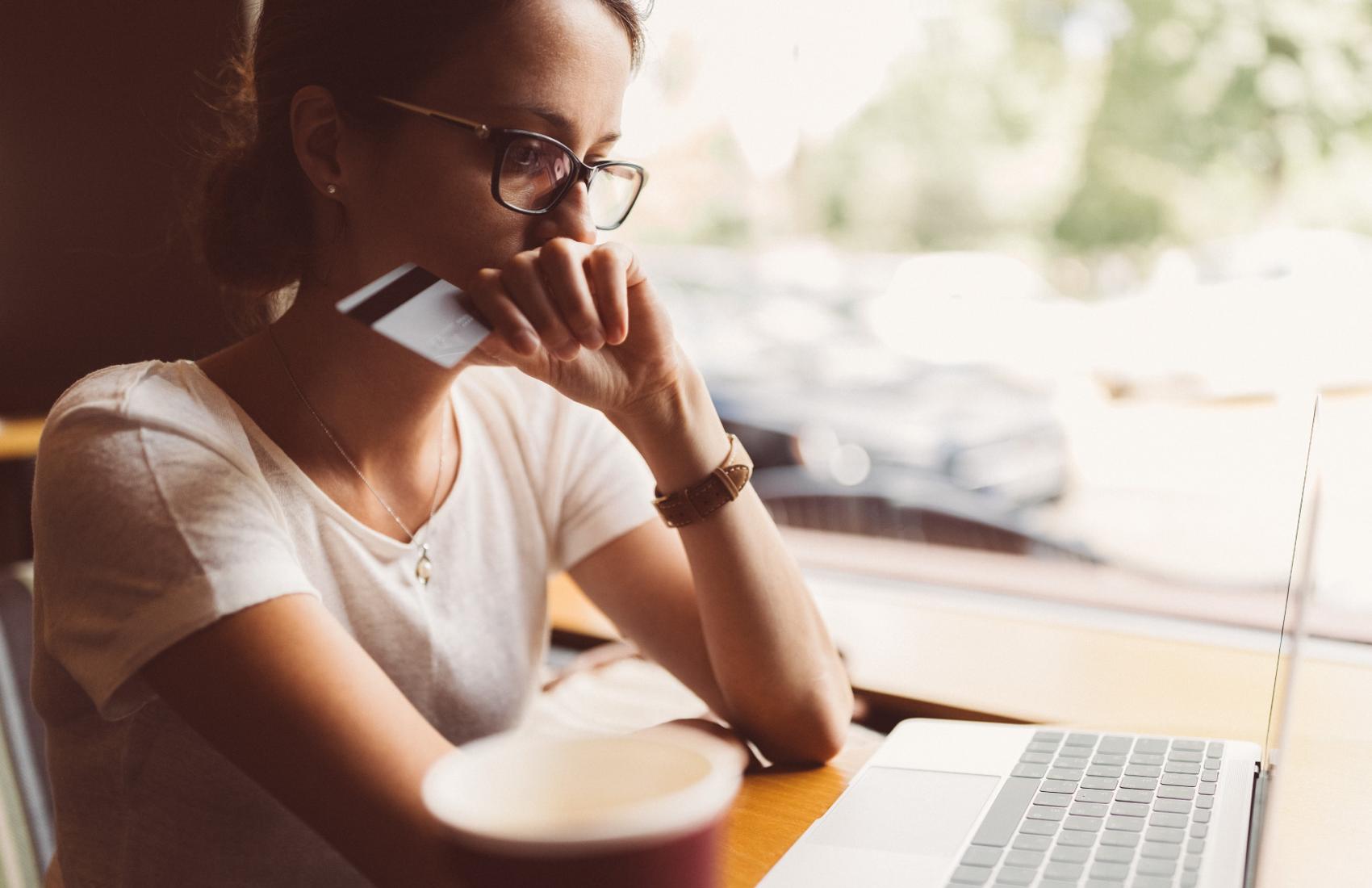 A woman sitting and holding a credit card looking at the laptop.