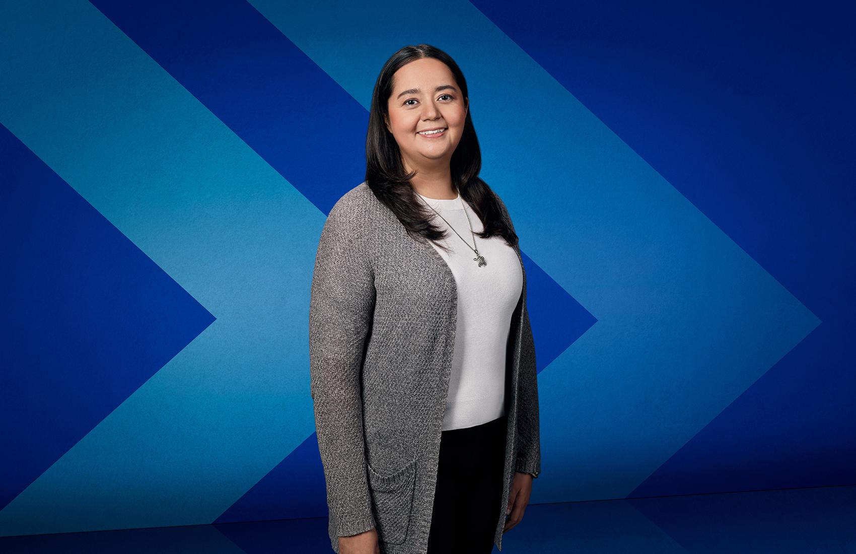 Dr. Johanna Sam, an assistant professor in UBC’s Faculty of Education and a citizen of the Tŝilhqot’in Nation, stands in front of a stylized chevron background