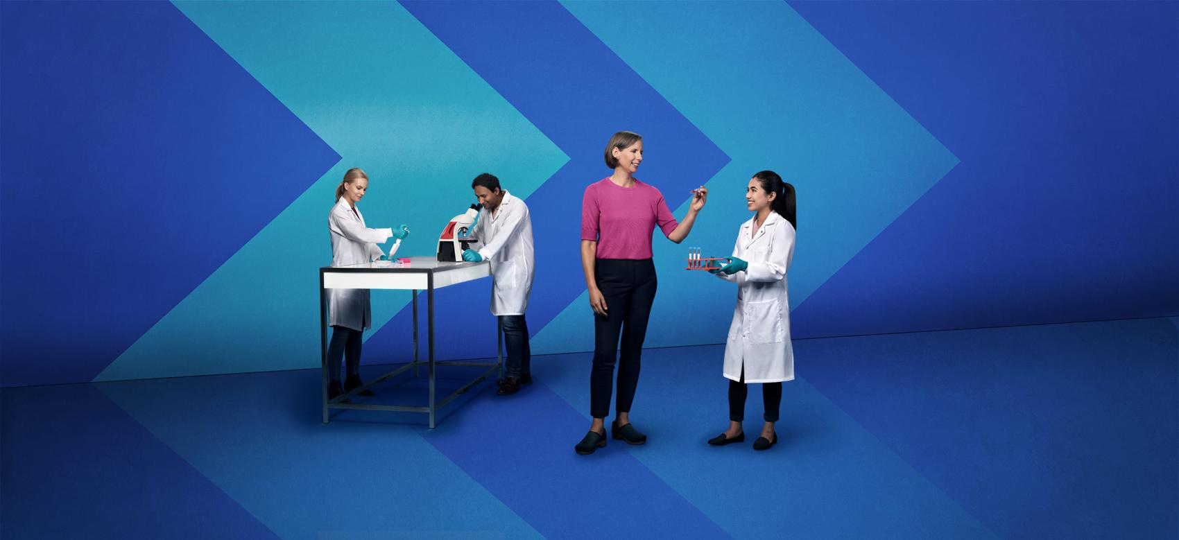 Three people in white lab coats and a person in a pink shirt working in a stylized lab with chevron backdrops.