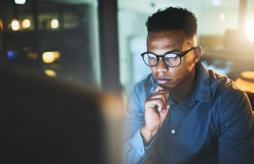 A person wearing glasses and a blue shirt stares at a desktop computer.