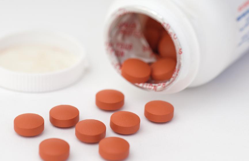 An opened bottle of medication with orange pills.
