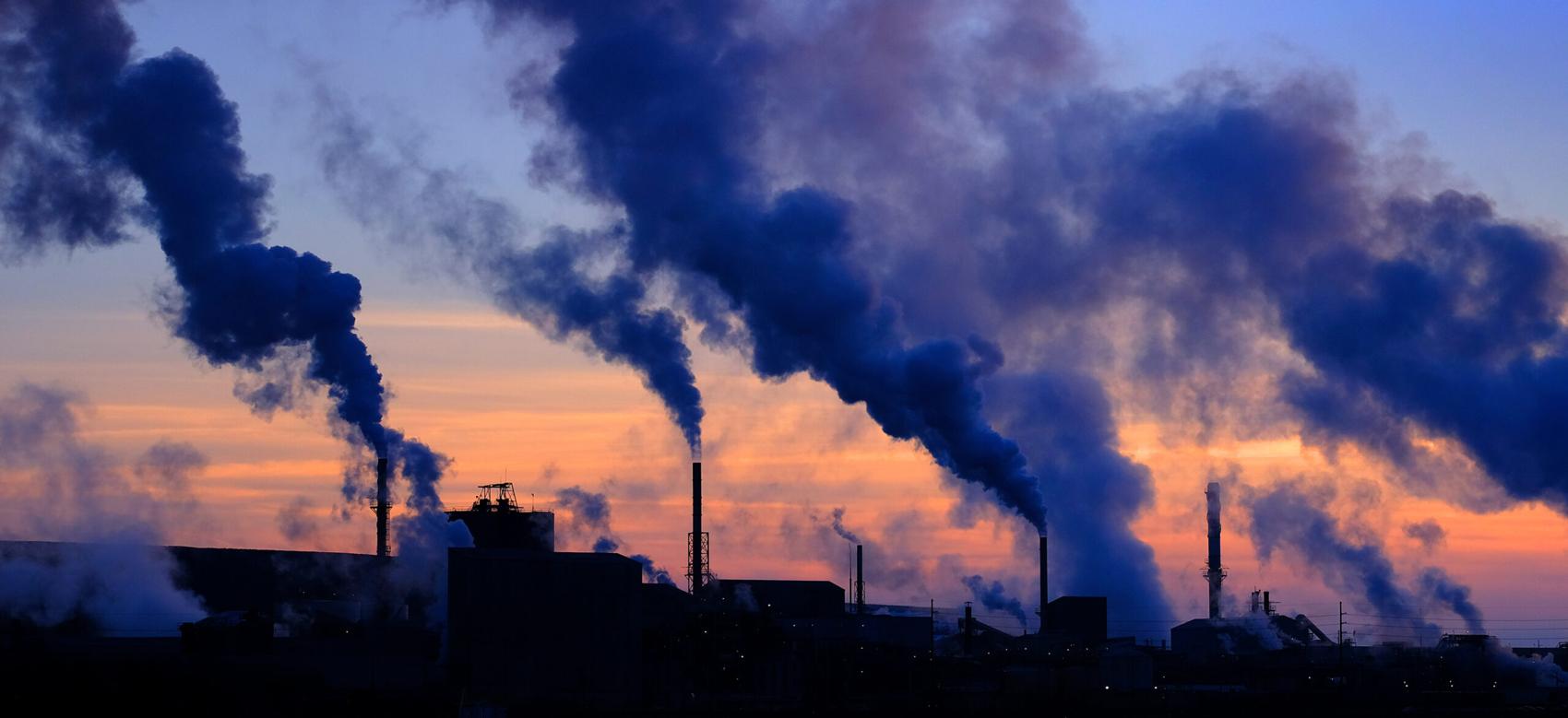 A photo of steam rising from smokestacks in a rural sunset sky.