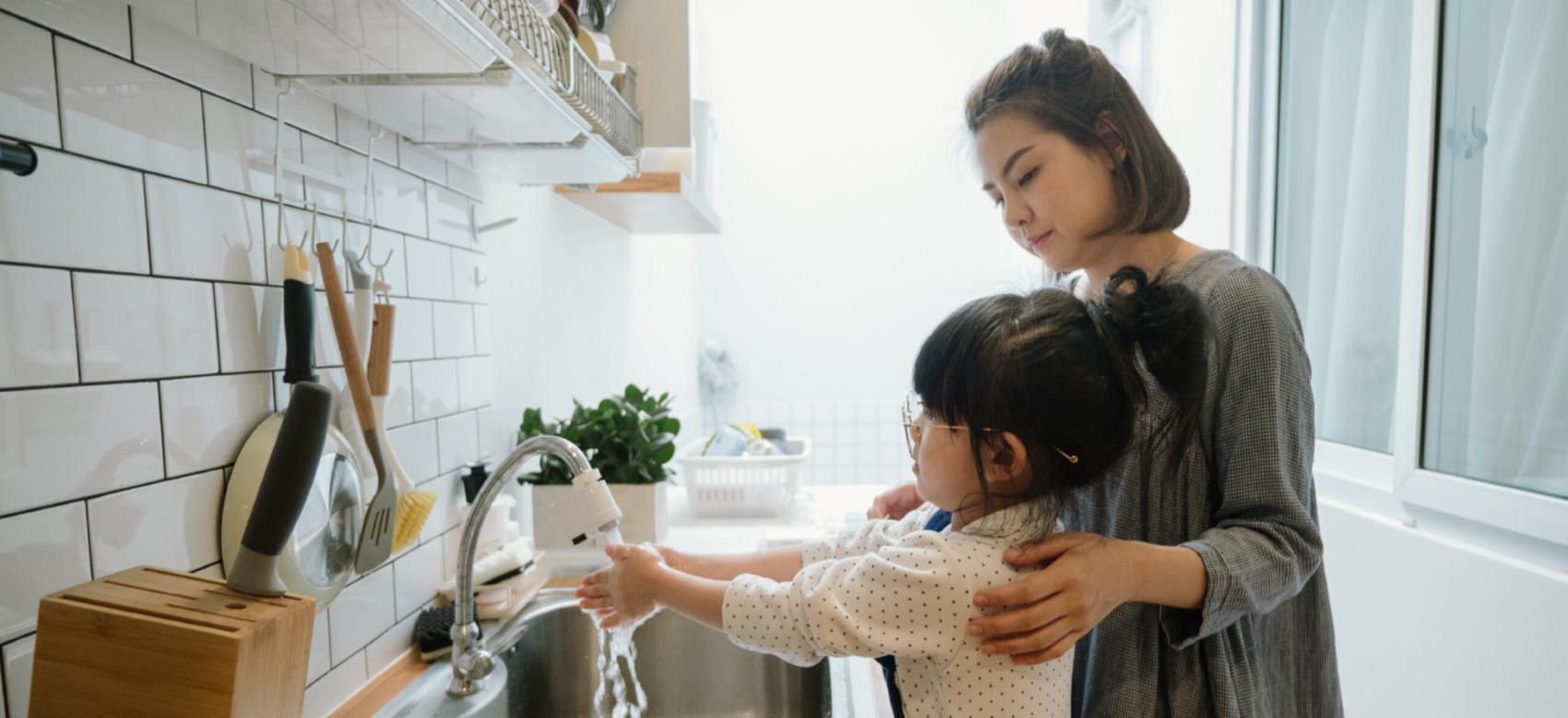 A mother observes her daughter washing her hands and teaches her about conserving water.