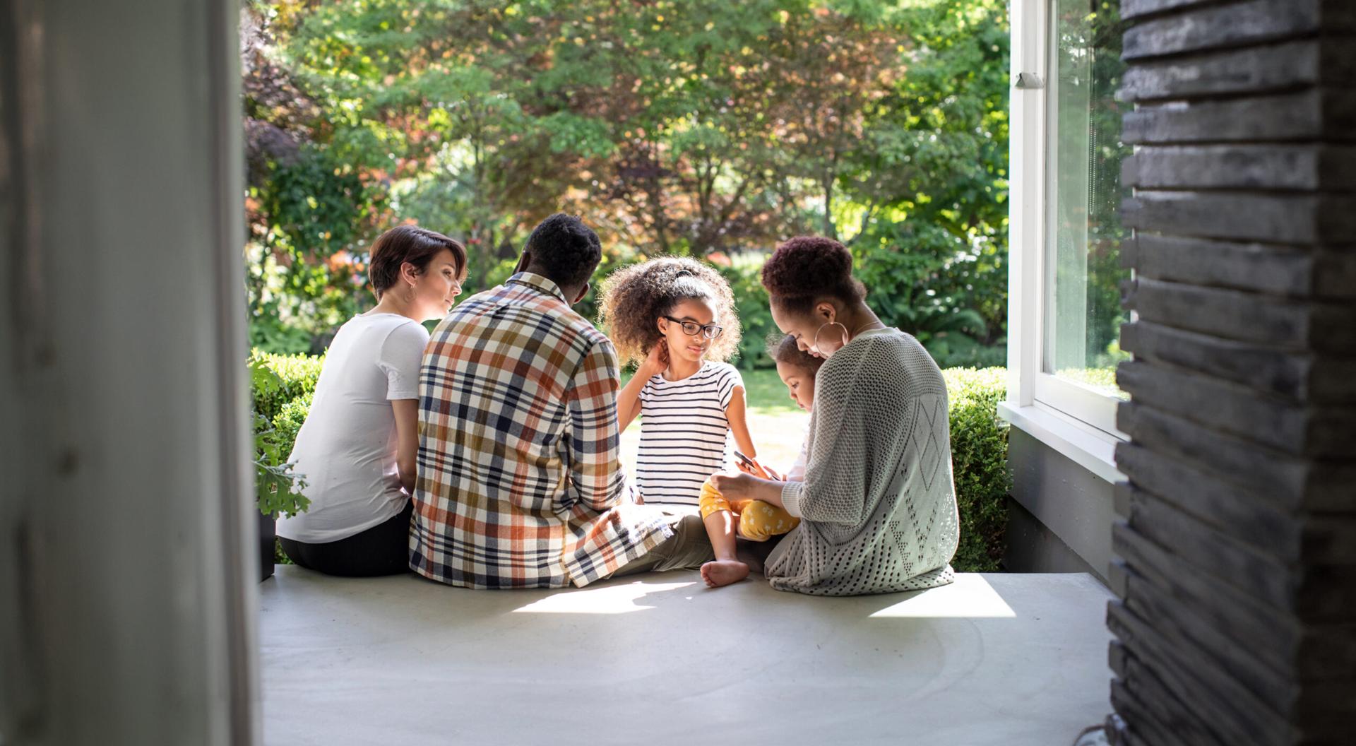 A black family with a mother, father and three daughters sit beside one another on the porch.