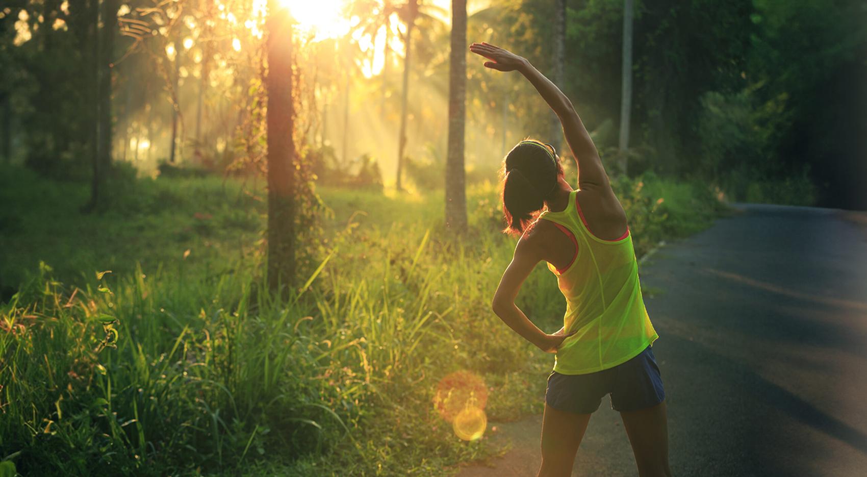 Young female runner warming up before running at morning forest trail