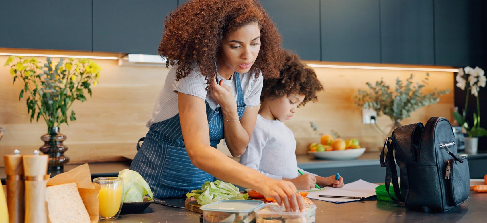 Mom in the kitchen with child, packing lunch while she is on the phone