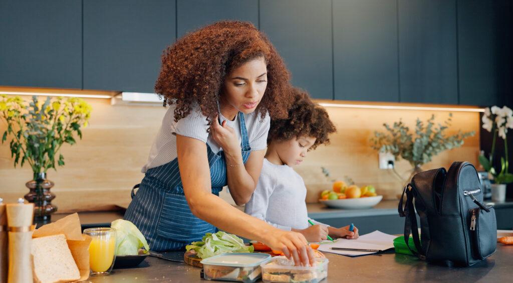 Mom in the kitchen with child, packing lunch while she is on the phone