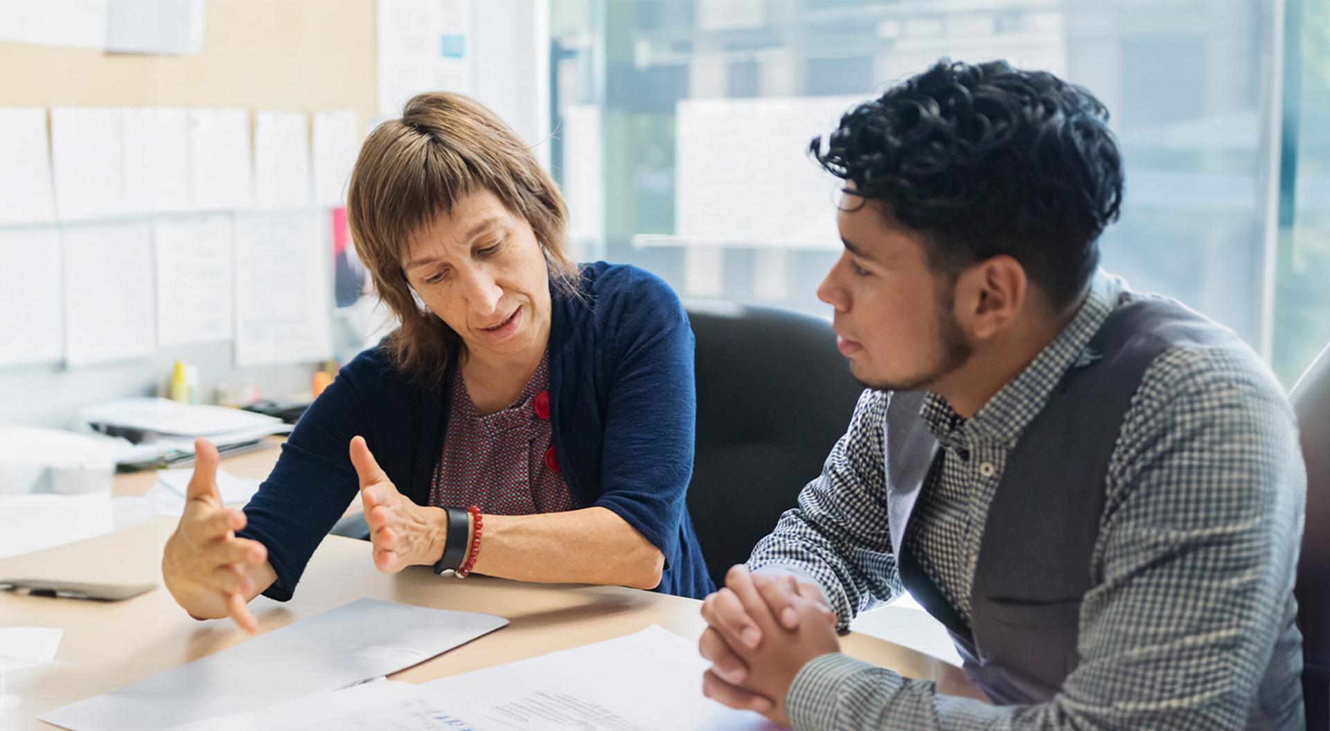A counselor is discussing matters with a young Latino man in the office.