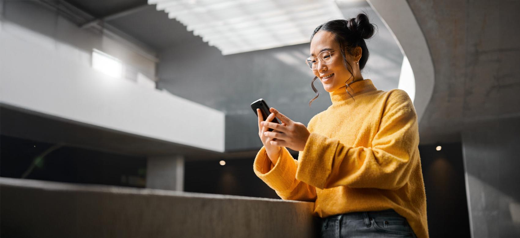 An Asian woman is smiling as she texts on her smartphone while reading it.