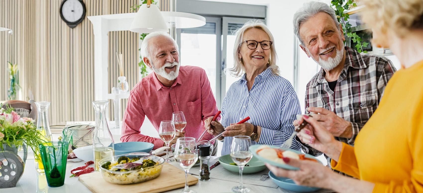 Four older adults smiling around a table of healthy food at home.