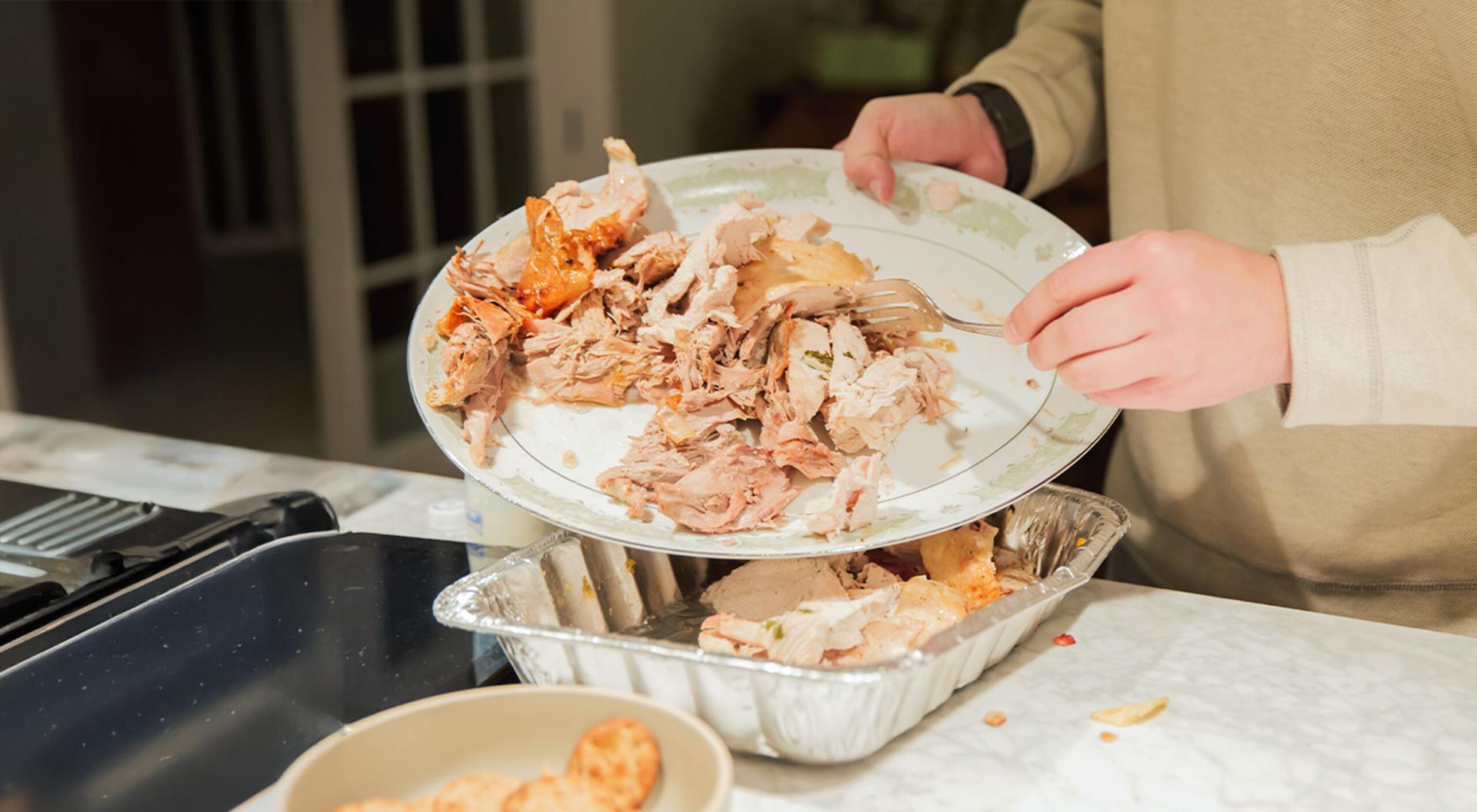 A woman is pouring leftover food from a plate into a tin tray.