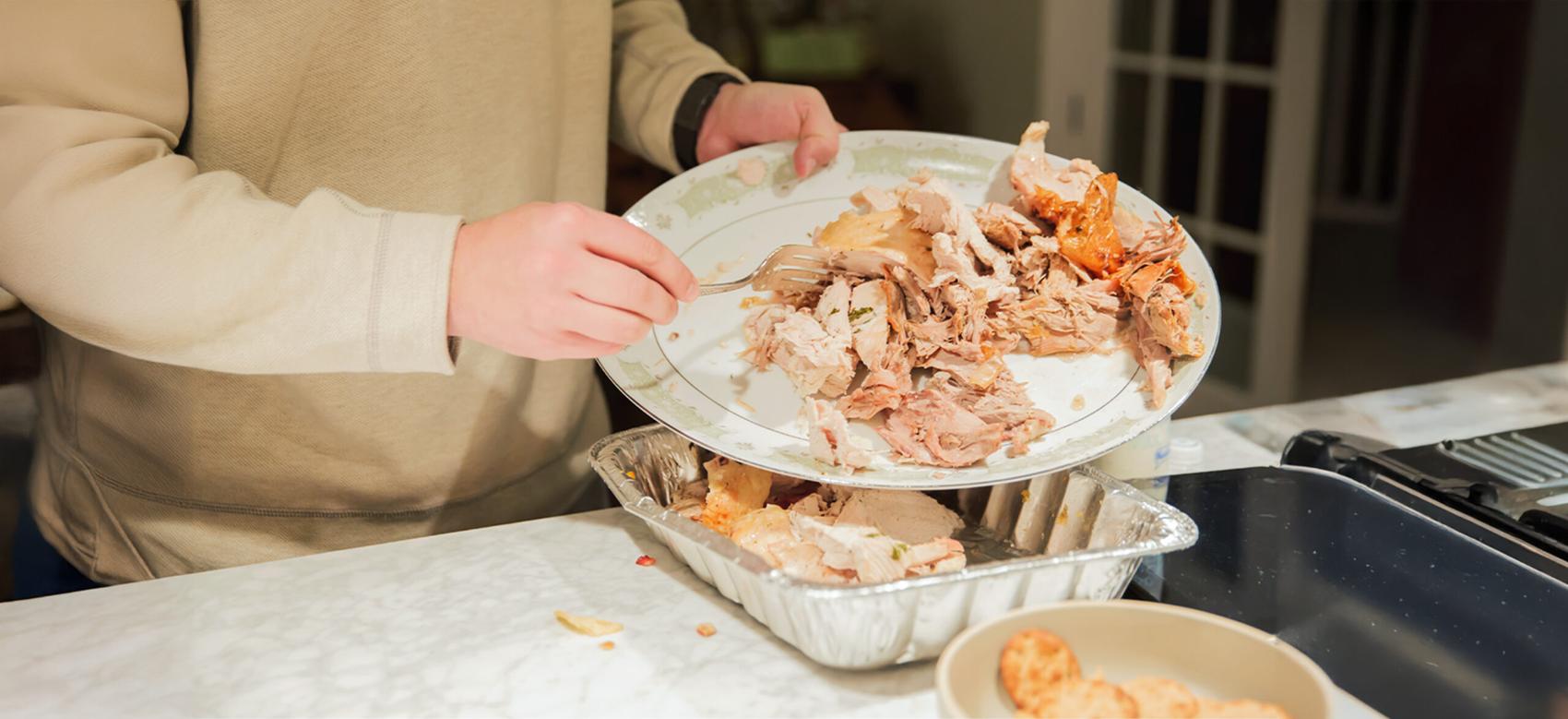 The woman is pouring leftover food from a plate into a tin tray.