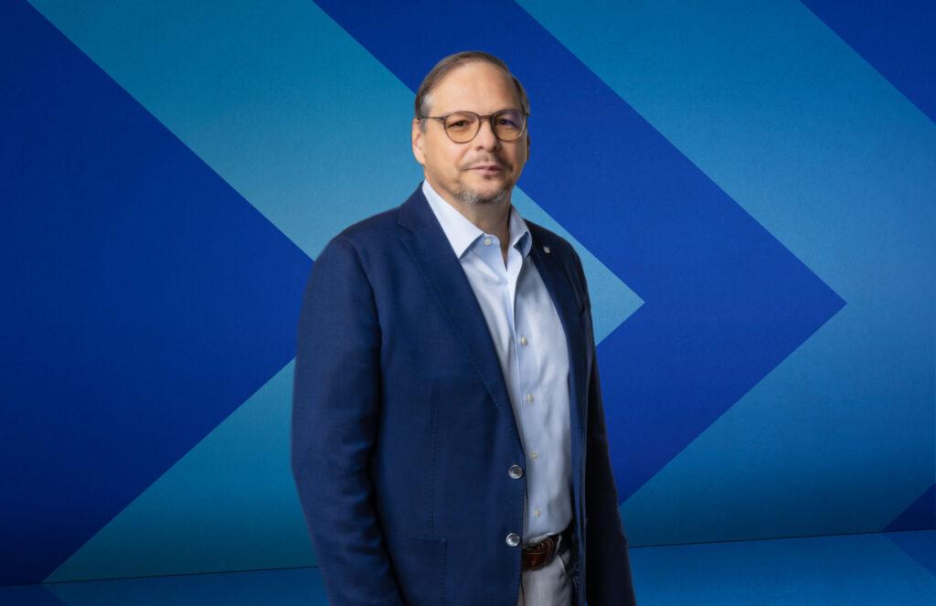 Dr. Orlando Rojas stands in front of a blue chevron background.