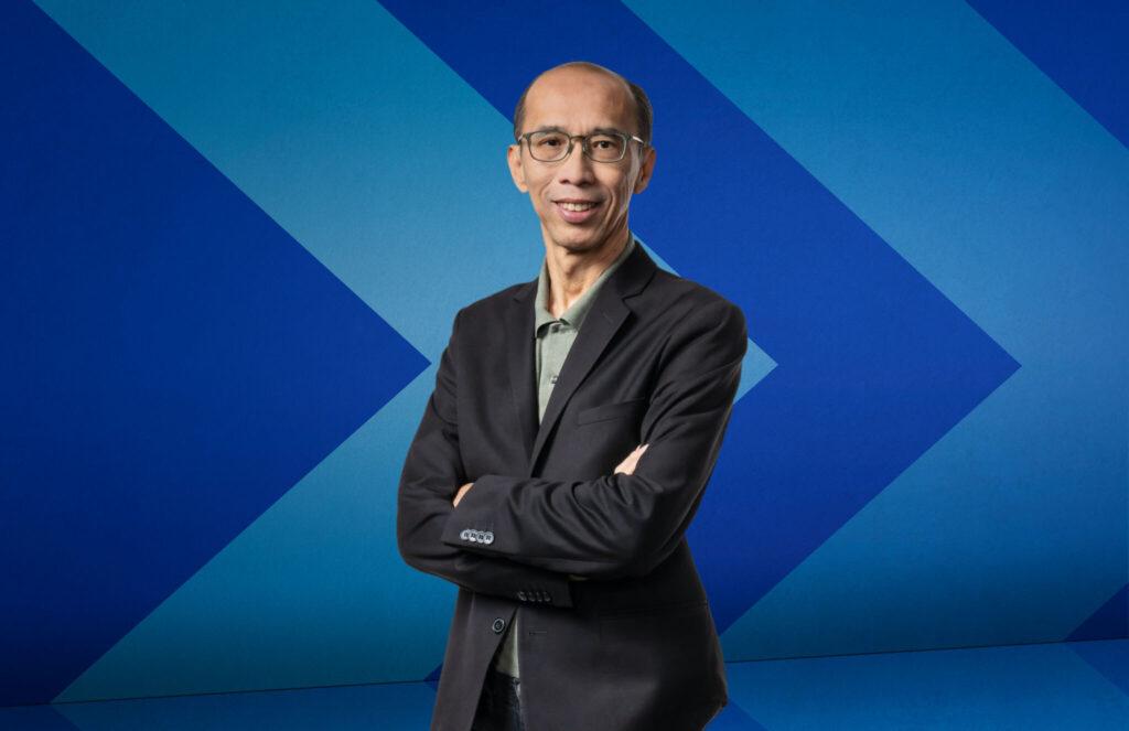Dr. Raymond Ng stands in front of a blue chevron background.